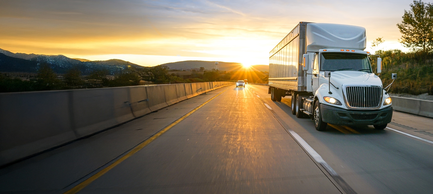 Red semi truck driving on interstate in sunset