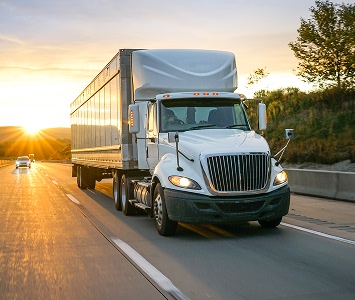 White semi driving on interstate with sunset