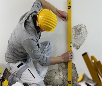 Contractor using a level to work on a wall with equipment near them