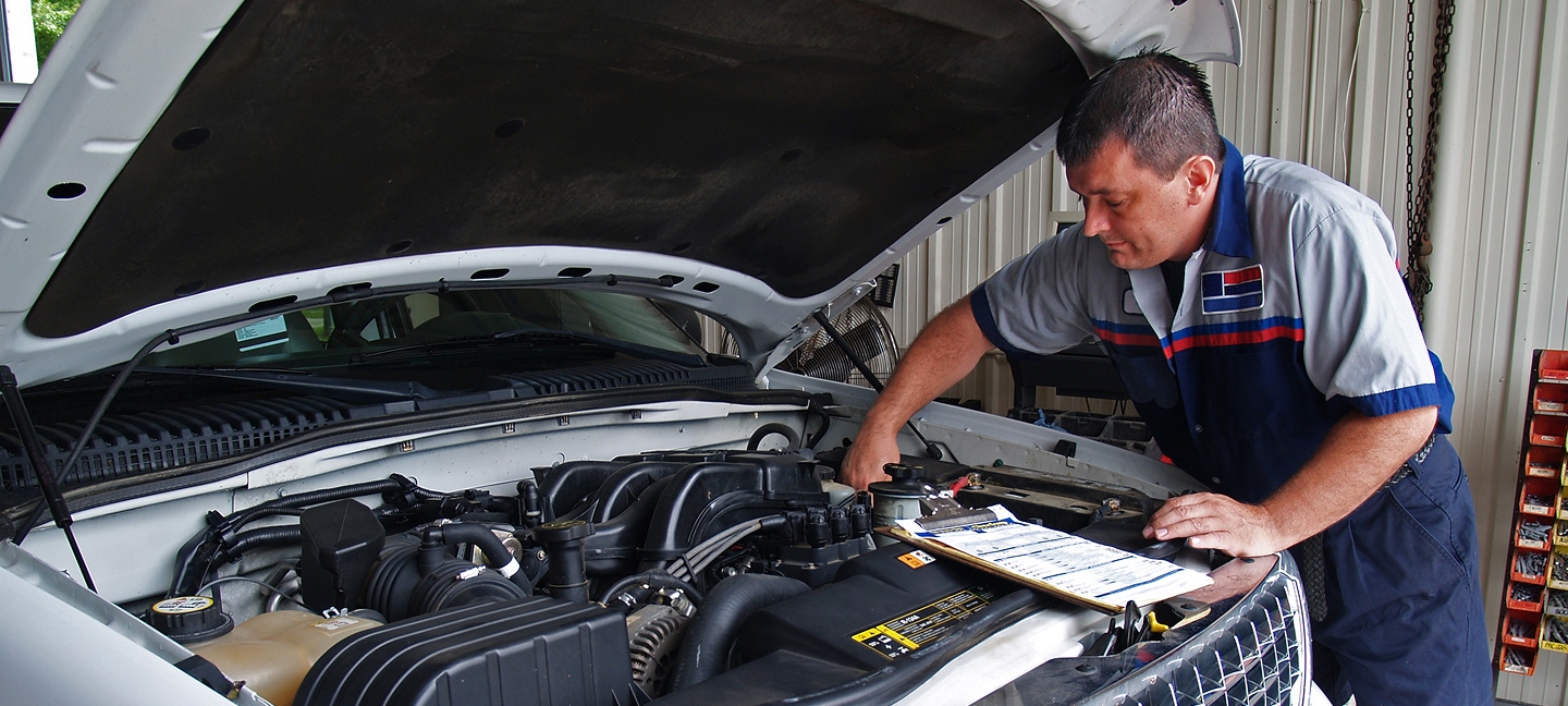 Man working on car engine with a clipboard
