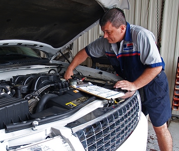 Man working on car engine with a clipboard